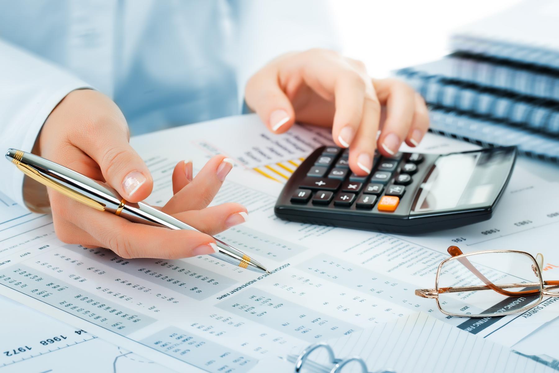 Hands of an accountant with calculator, financial statements, and notes on a desk